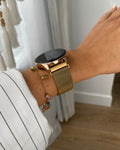 Gold smartwatch and bracelet on a wrist with a blurred background