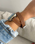 Person wearing a smartwatch with a brown leather strap on a neutral background