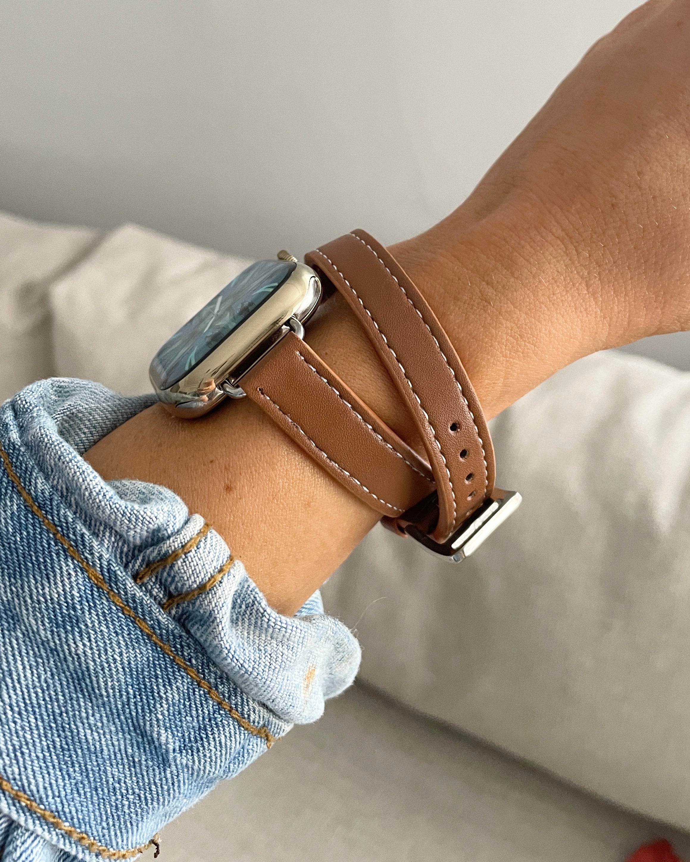 Person wearing a smartwatch with a brown leather strap on a neutral background