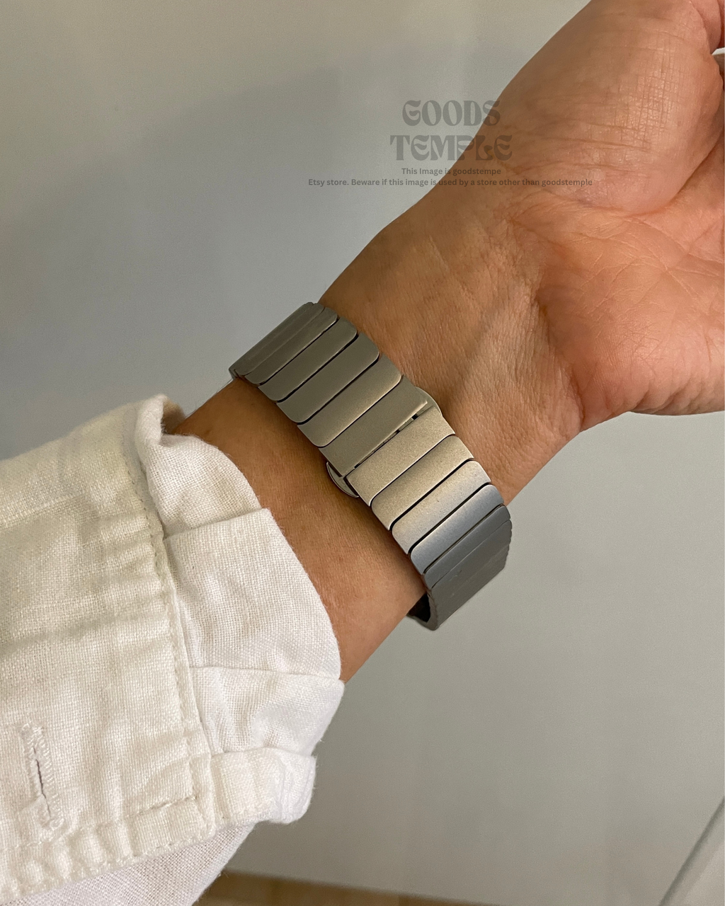 Hand wearing a silver metal bracelet against a neutral background