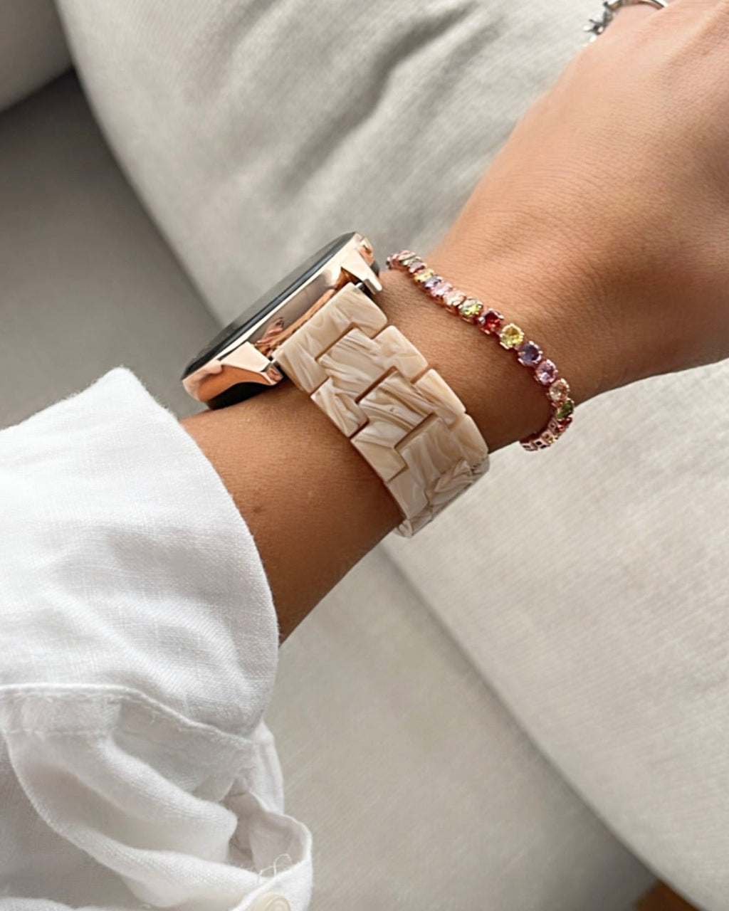 Close-up of a wrist wearing a watch and bracelets on a neutral background