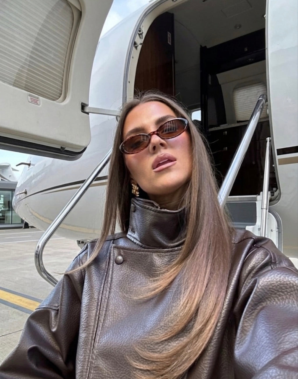 Person wearing a leather jacket and sunglasses in front of a private jet