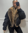 Person wearing a black jacket with a fur-lined hood against a plain background