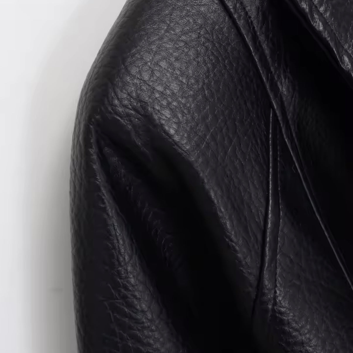Close-up of a black pebbled leather jacket showing the texture and fold details against a plain white background.