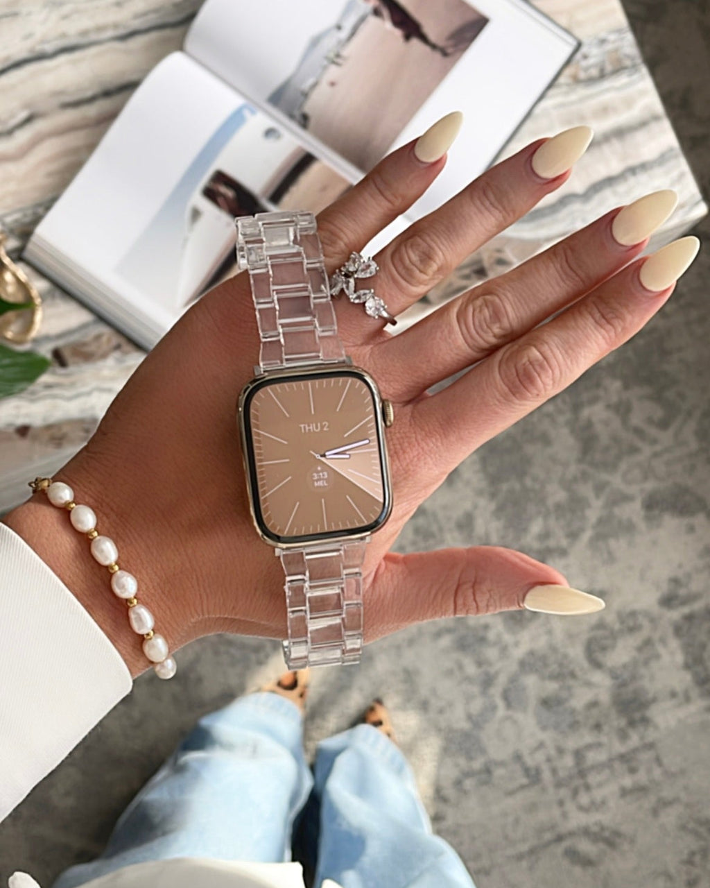 Hand wearing a silver watch with a clear strap on a textured surface
