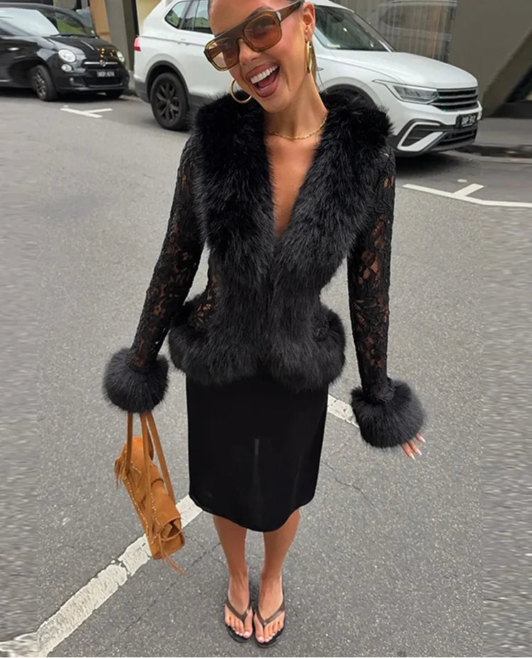 A woman wearing a black lace long-sleeve vest with fluffy faux fur trim and cuffs, paired with a black skirt, sunglasses, and a tan handbag, standing on a city street.