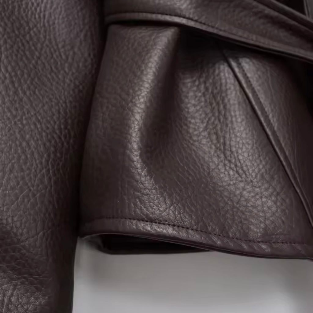Close-up of a dark brown pebbled leather garment, showing the texture and fold details of the fabric.