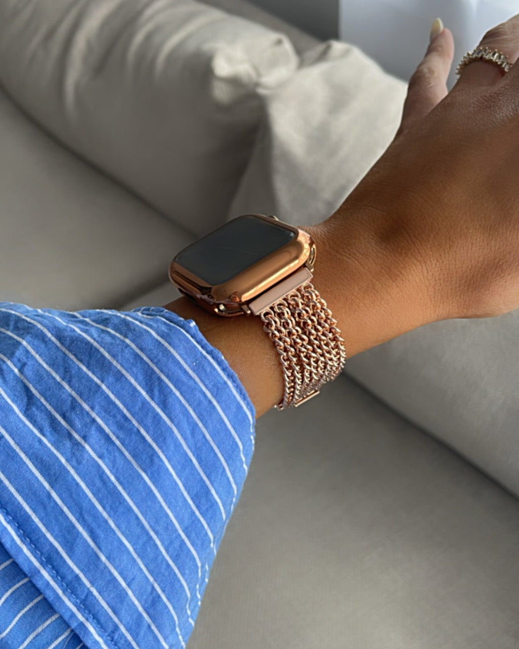 Person wearing a smartwatch with a rose gold band on a light-colored couch.