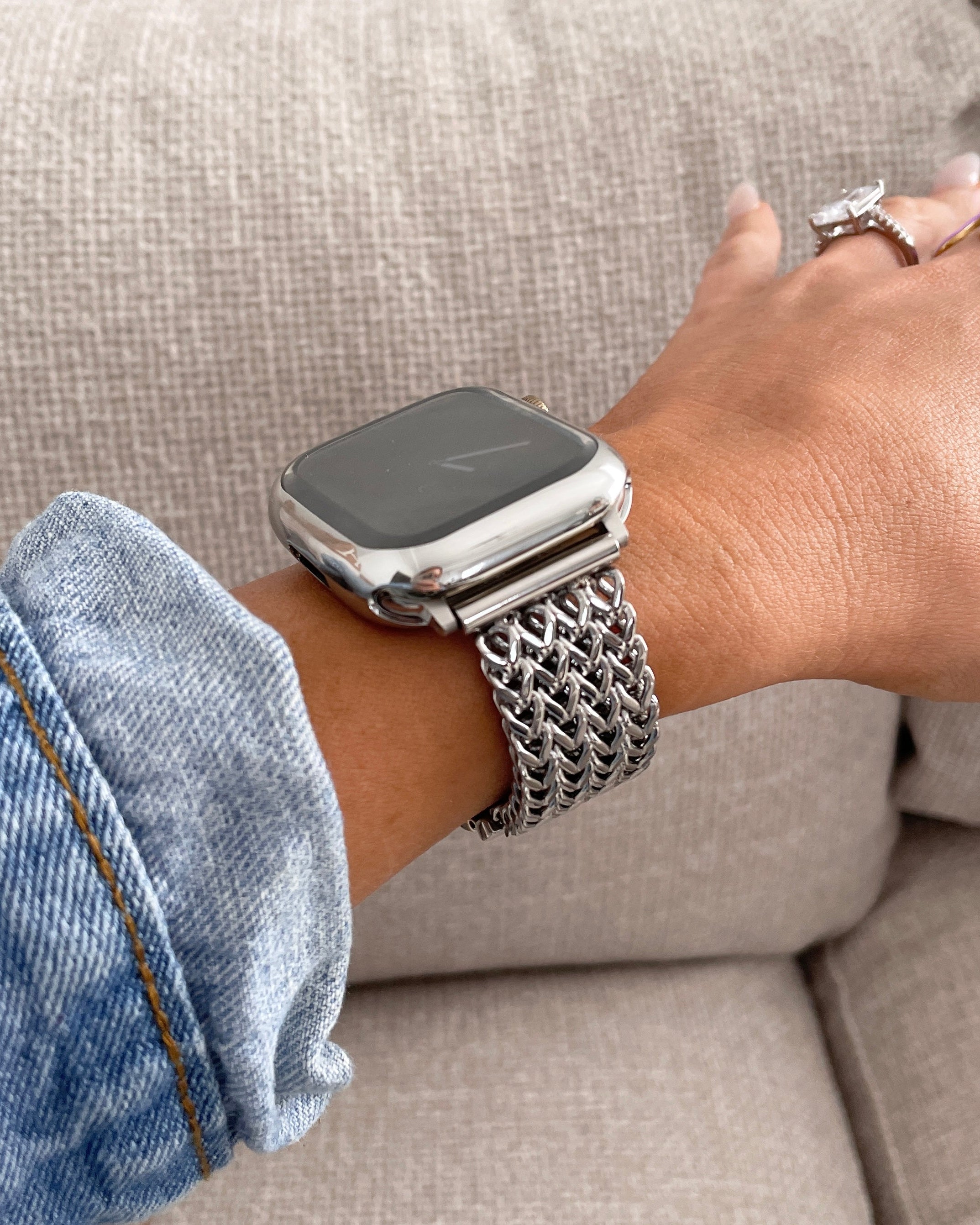 Person wearing a silver smartwatch with a chain strap on a neutral background
